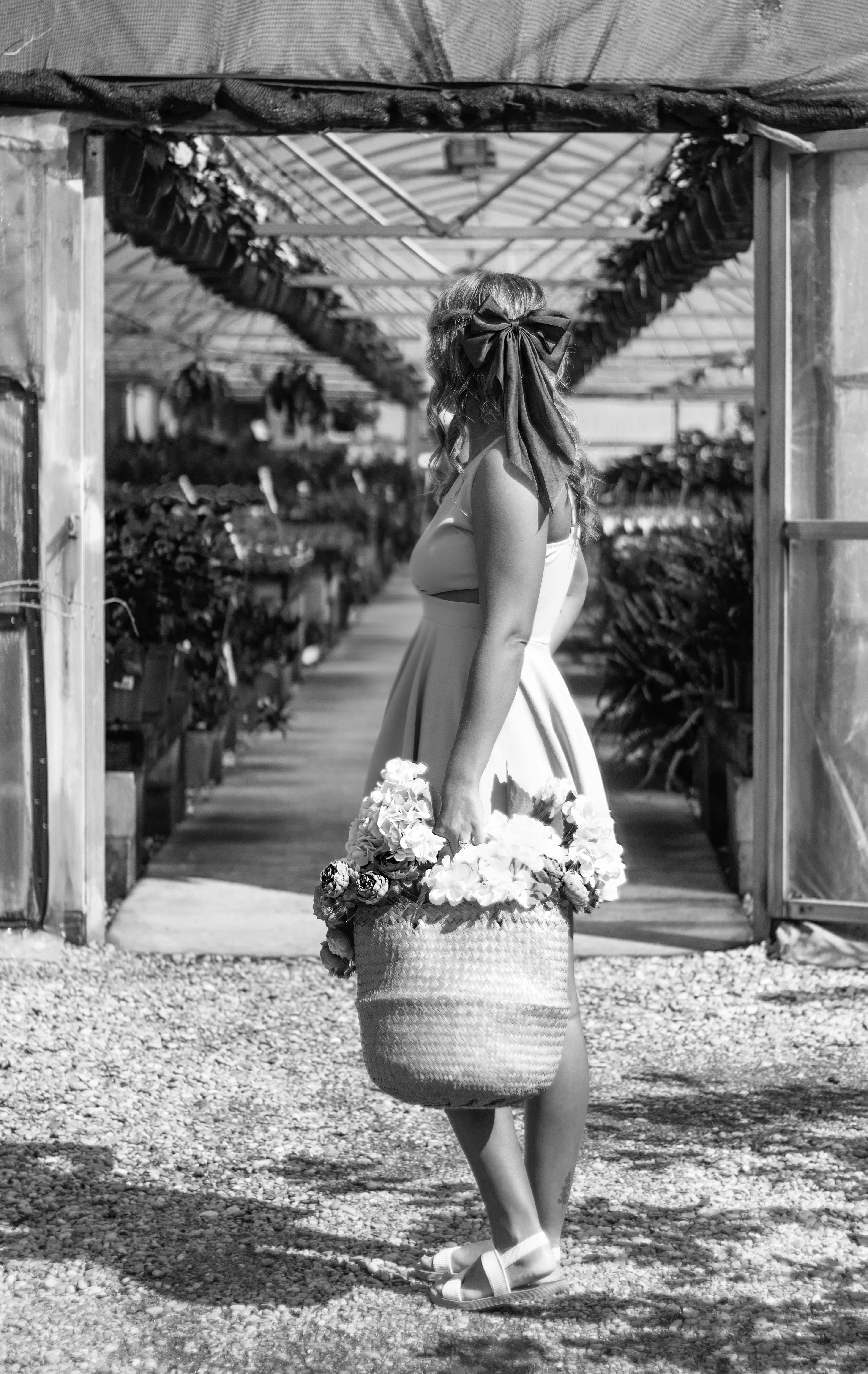 Black and white image of a woman in a greenhouse holding a basket of flowers.