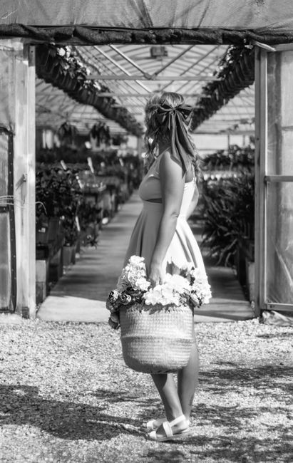 Black and white image of a woman in a greenhouse holding a basket of flowers.