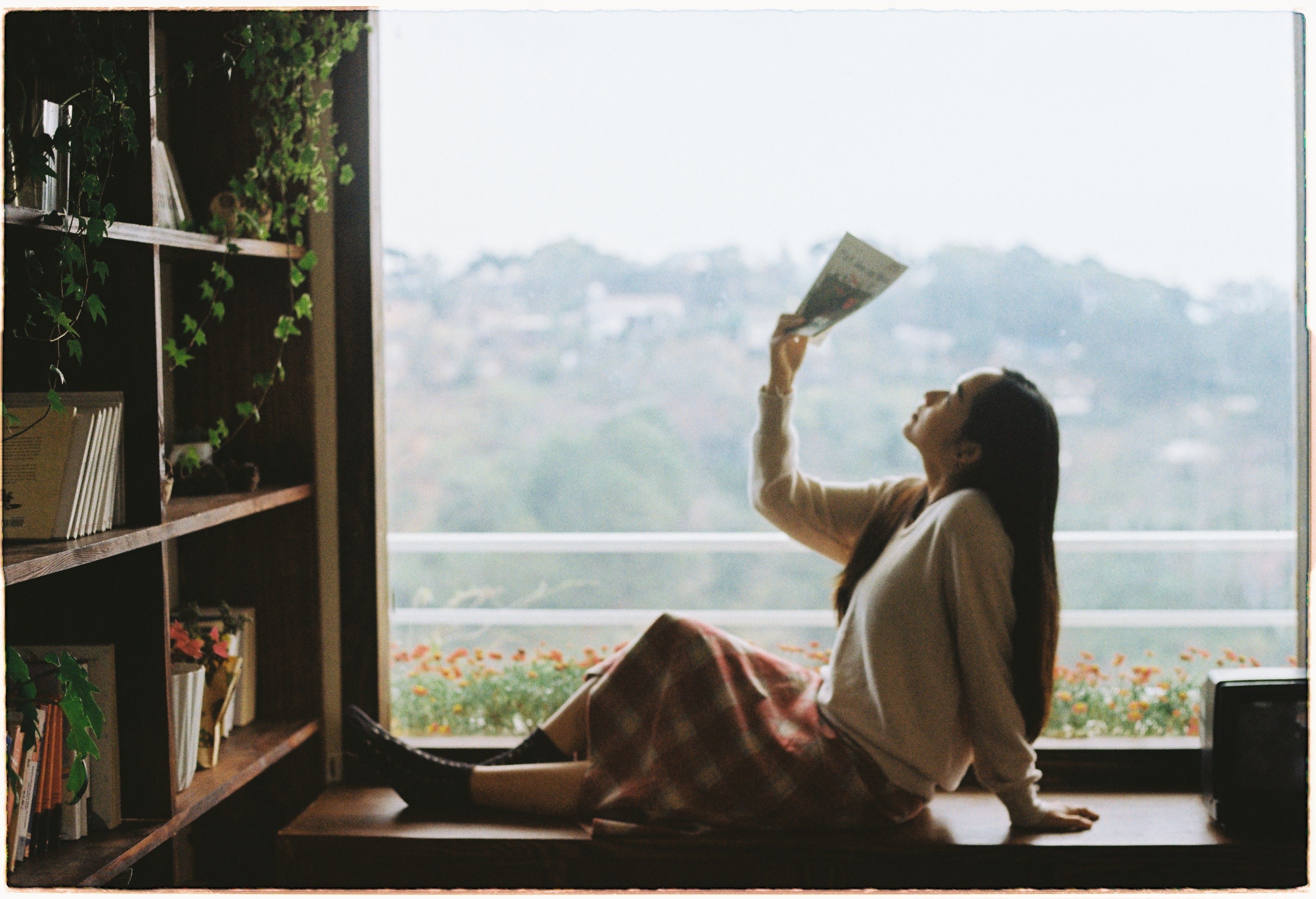 A serene image of a woman reading a book while seated by a window with a view of the mountains.