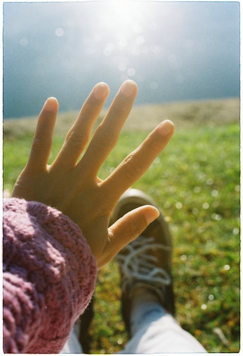 A person's hand is in the grass with the sun in the background