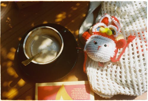 A crocheted toy sitting on a table next to a cup of coffee
