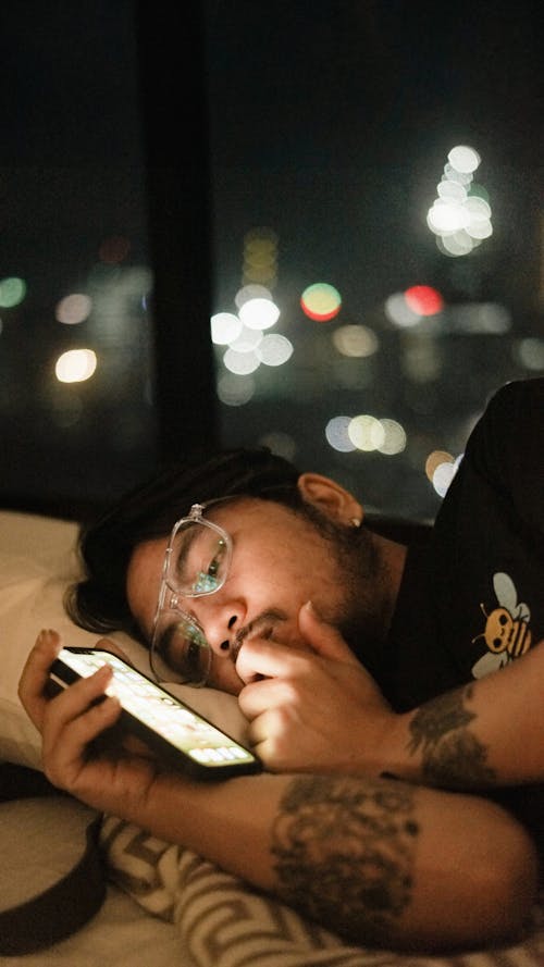 A man laying in bed with his eyes closed and holding a cell phone