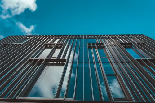Free Low angle view of a modern architectural office building with reflective windows under a clear blue sky. Stock Photo