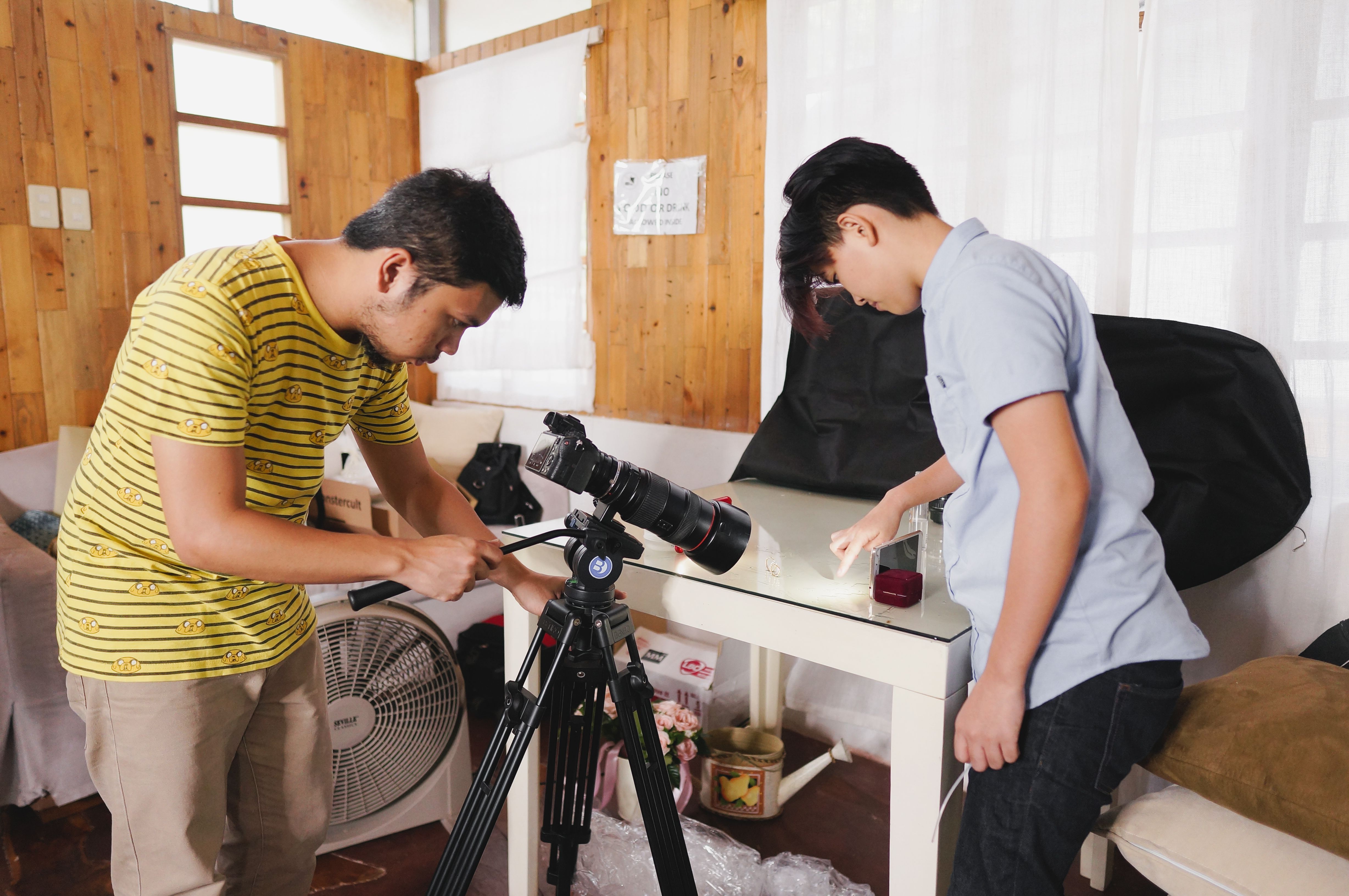 Two photographers working with camera equipment indoors, adjusting setup.