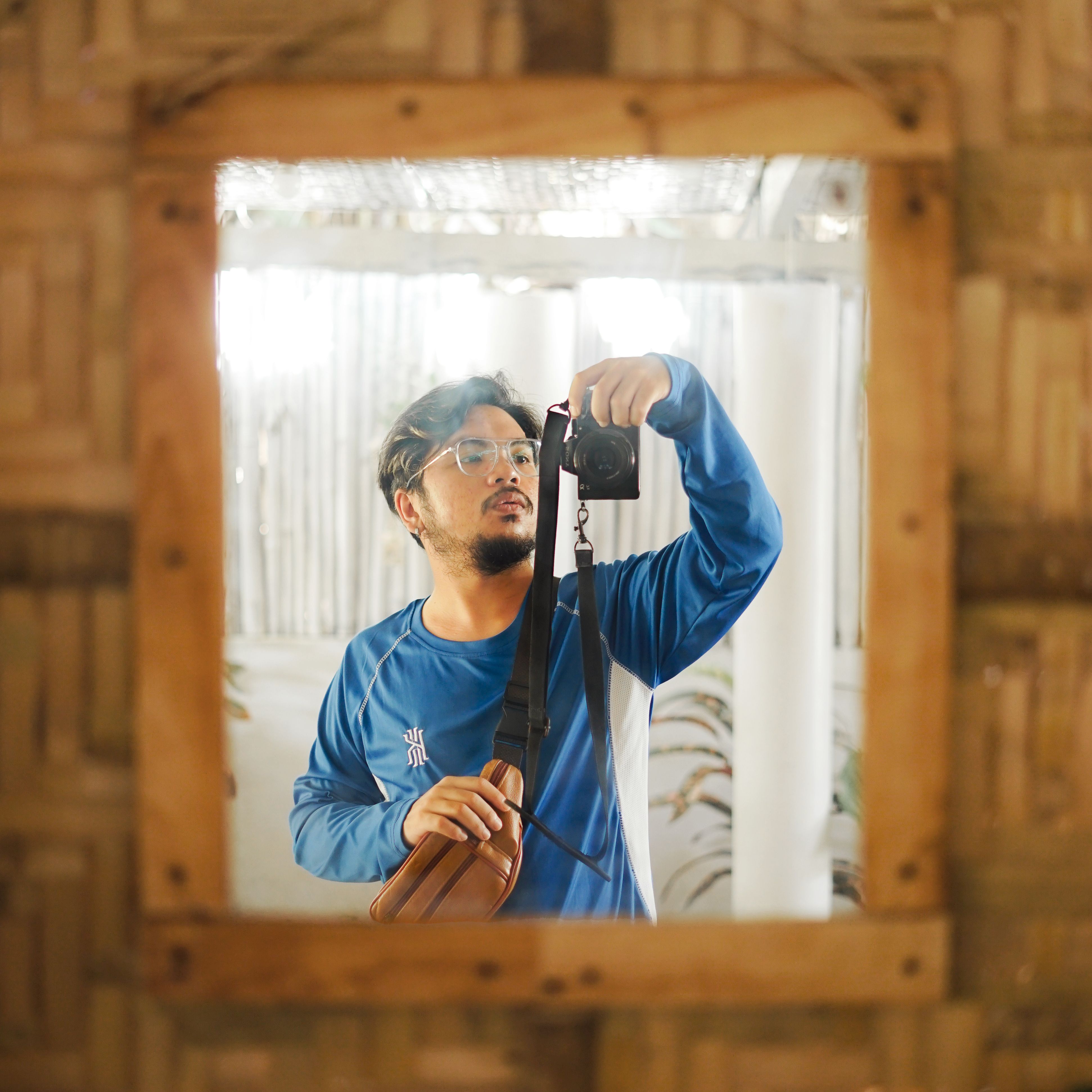 A man in a blue shirt captures a mirror selfie with a digital camera, focusing on reflection.