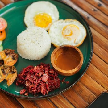 Top view of a traditional Filipino breakfast with rice, egg, and side dishes on a green plate.