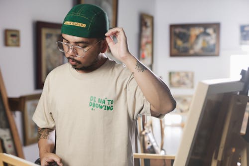 A man in a green hat is standing in front of a painting