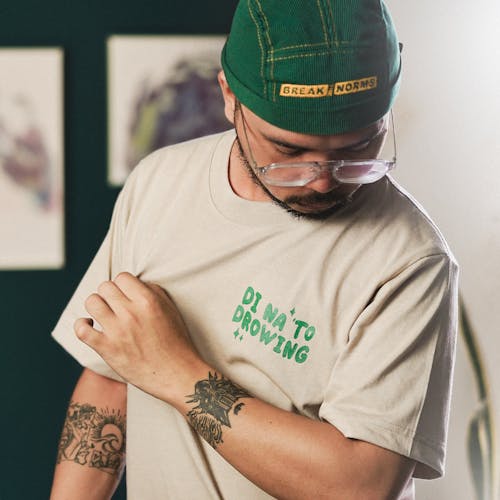 A man with tattoos and a green hat is wearing a t - shirt that says, to grow