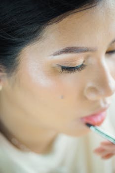 Detailed portrait of a woman applying makeup, highlighting beauty and precision.