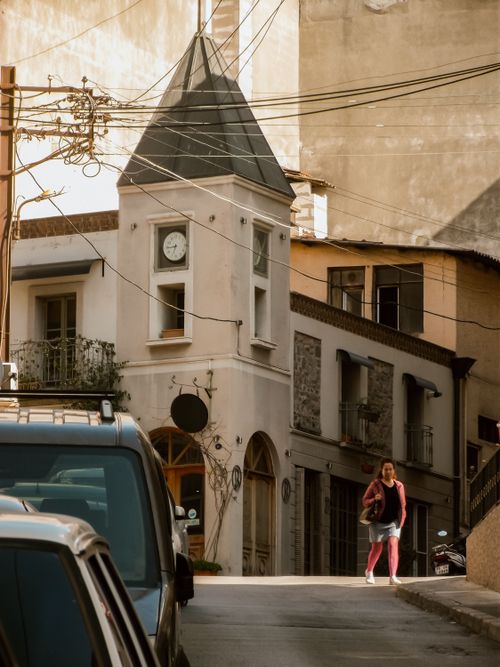 Free Woman walking in an old town street with a vintage clock tower at sunset. Stock Photo