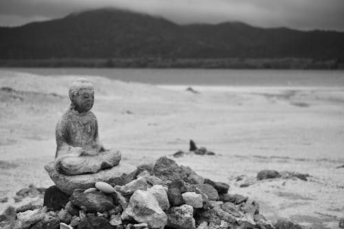 Free Black and White Photo of a Statue of Buddha and a Pile of Rocks on a Beach  Stock Photo