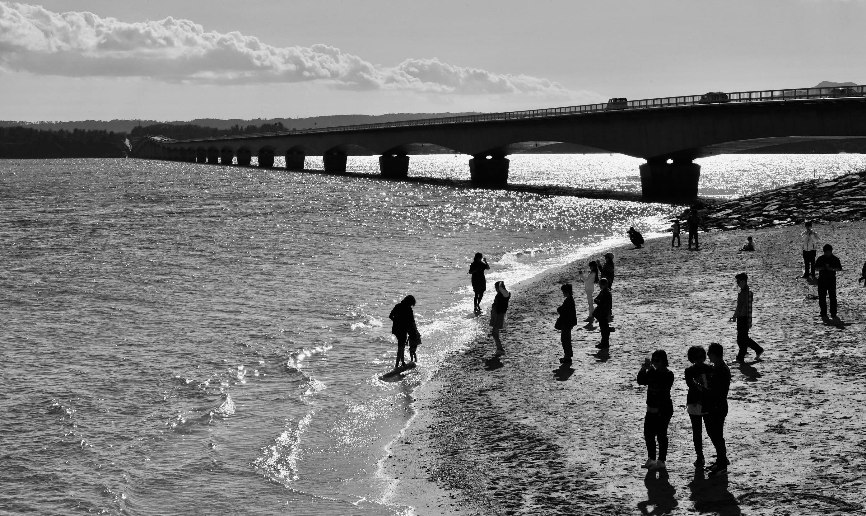 Captivating black and white scene of people enjoying a summer day by an Okinawa bridge.
