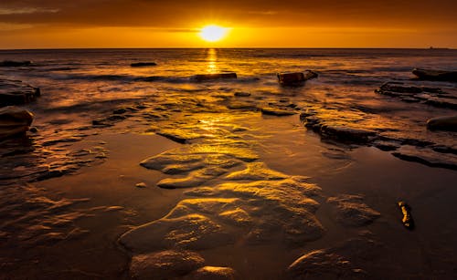 A sunset over the ocean with rocks and water