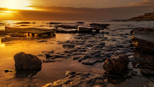 A sunset over the ocean with rocks and water