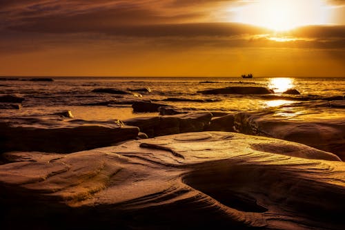 A sunset over the ocean with rocks and water