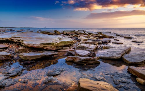 A sunset over the ocean with rocks and water