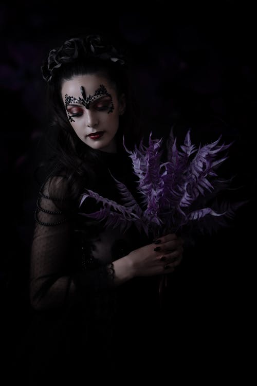 A woman in black and purple makeup holding a purple flower