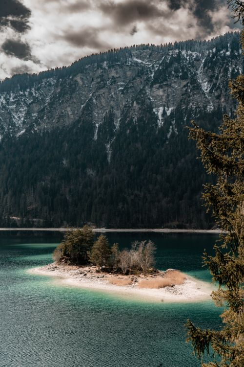 Free Stunning vertical shot of Eibsee Lake with an island and snowcapped Bavarian Alps backdrop. Stock Photo