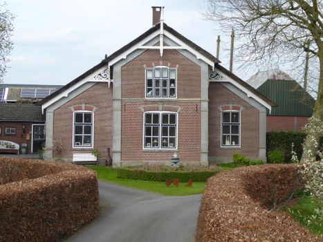 A peaceful brick house surrounded by countryside hedges under a clear sky.