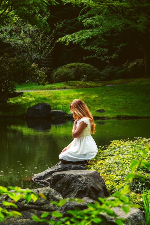 A woman in white dress sitting on rocks by pond