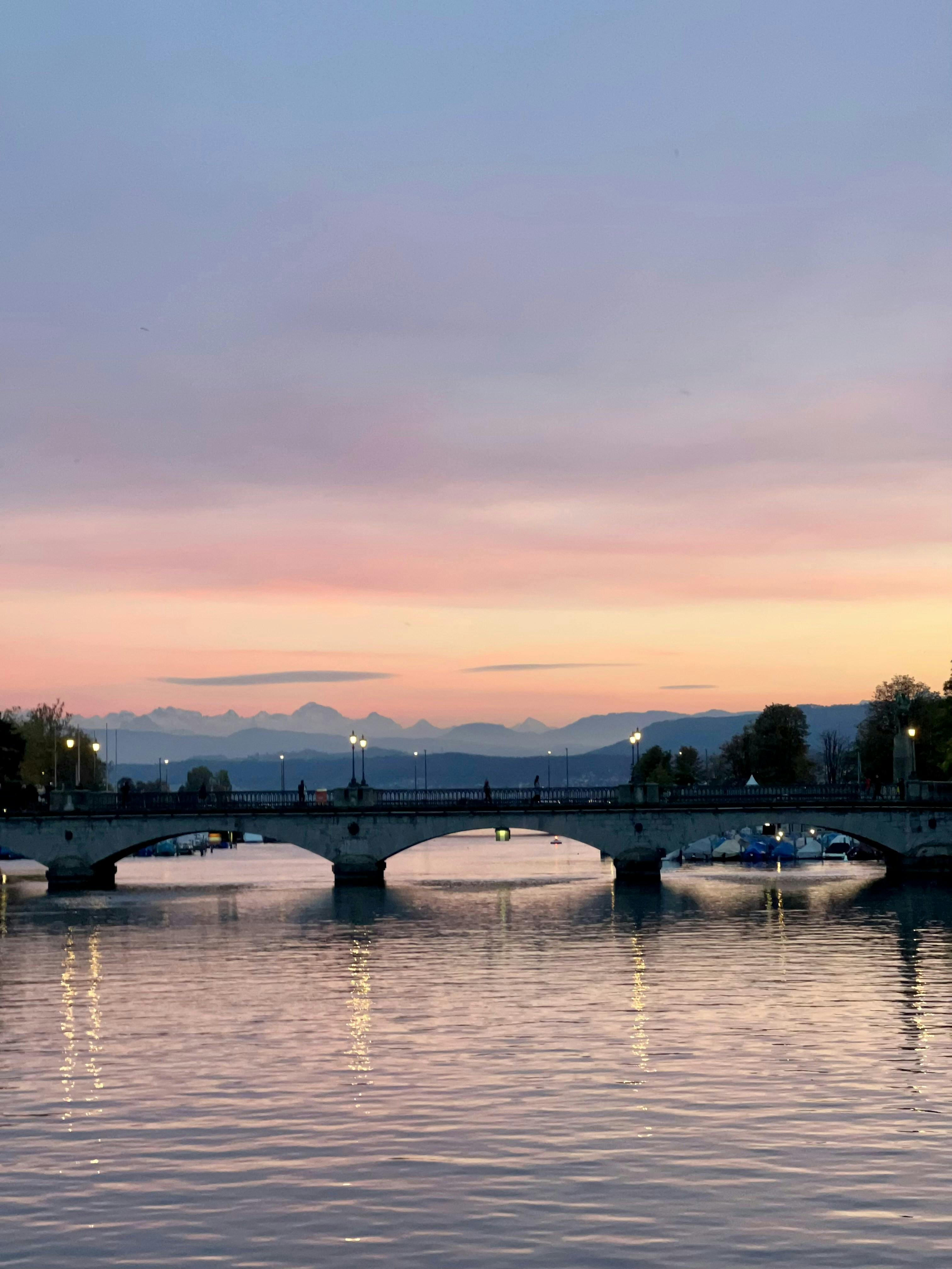 Münsterbrücke in Zürich at sunset, reflecting in the Limmat River, creating a serene evening view.