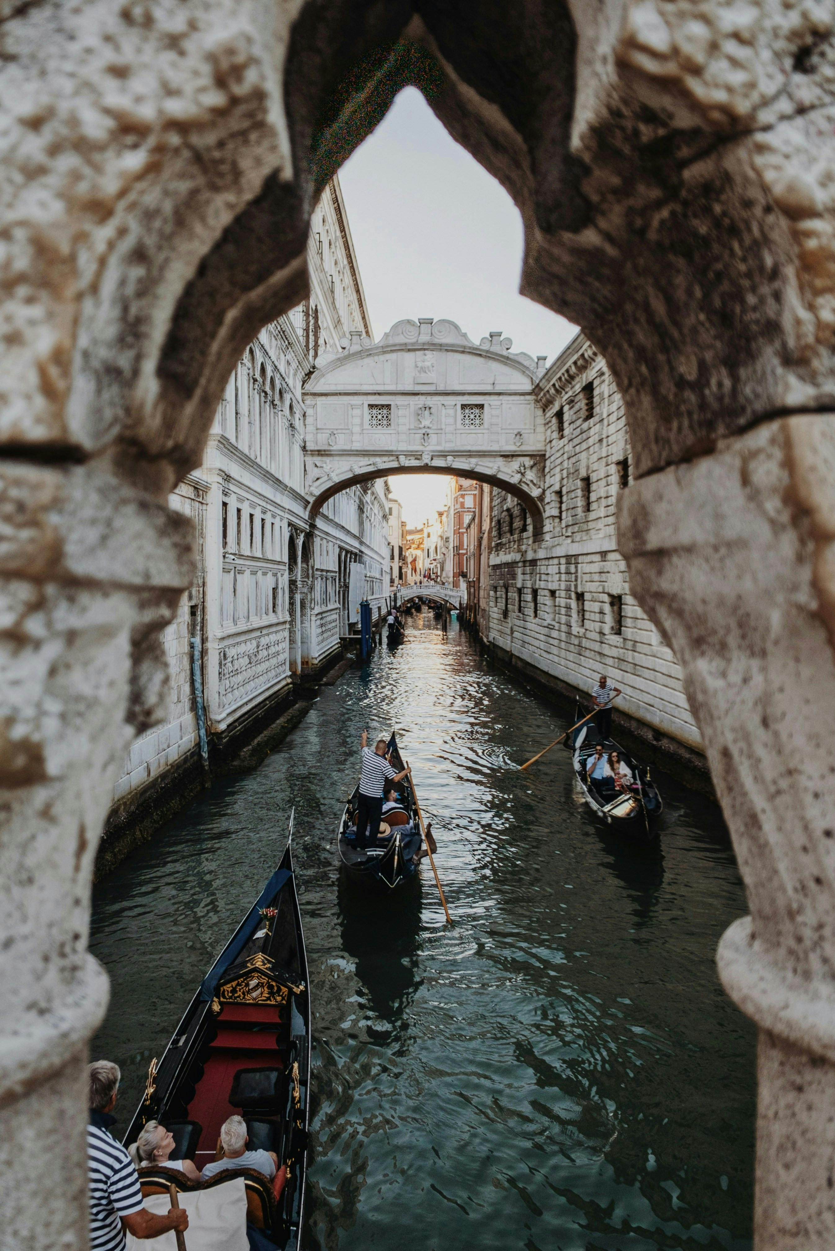 A captivating view of gondolas passing beneath the historic Bridge of Sighs in Venice, Italy, framed by stone arch.