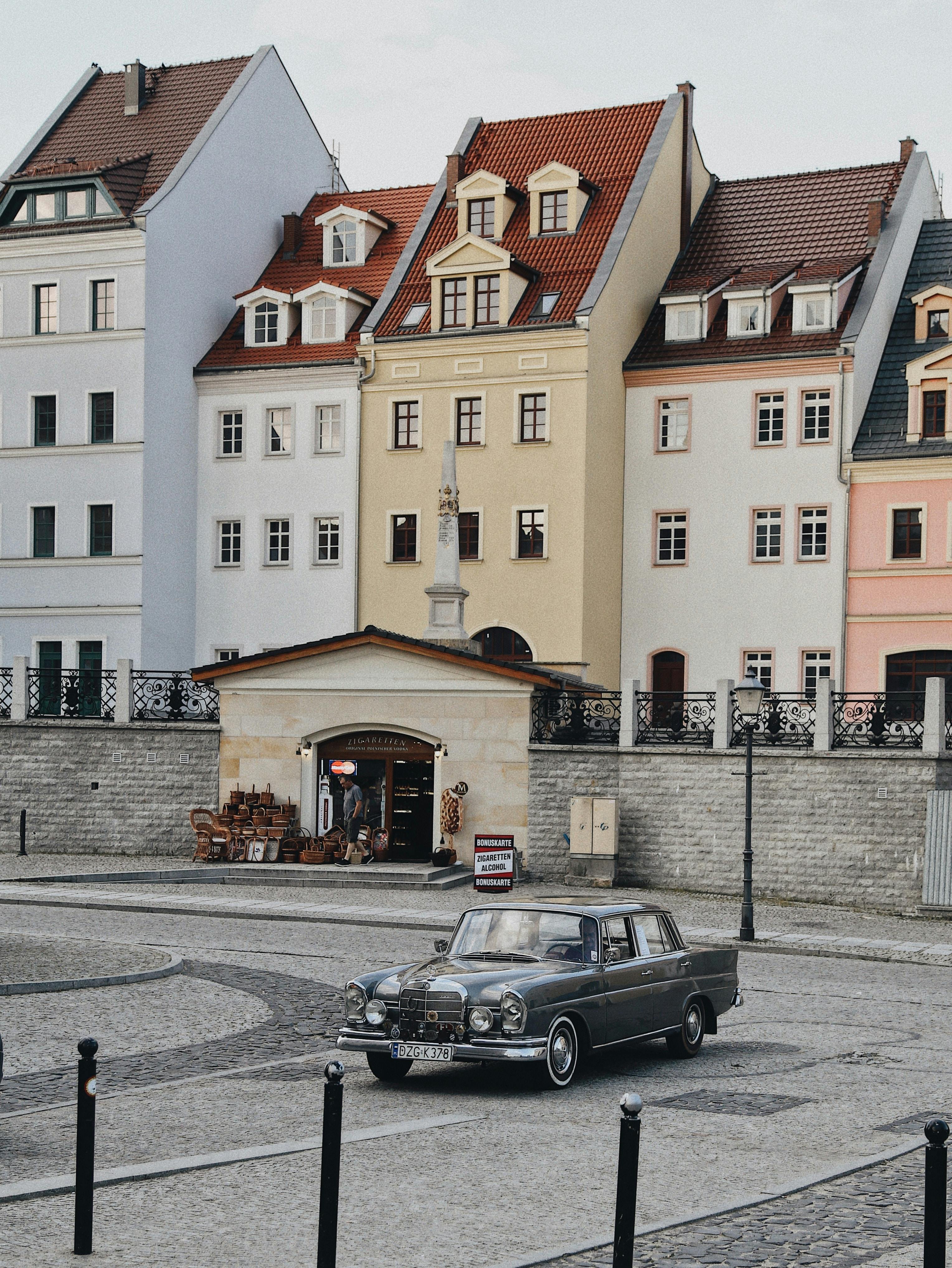 A classic car parked in front of colorful vintage townhouses in an urban setting.