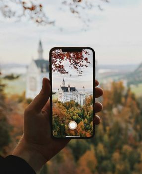 Photo of Neuschwanstein Castle through smartphone, showcasing autumn scenery.