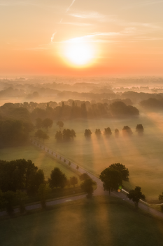 Aerial view of lush fields at sunrise with mist and warm sunlight in Fluitenberg, Netherlands.