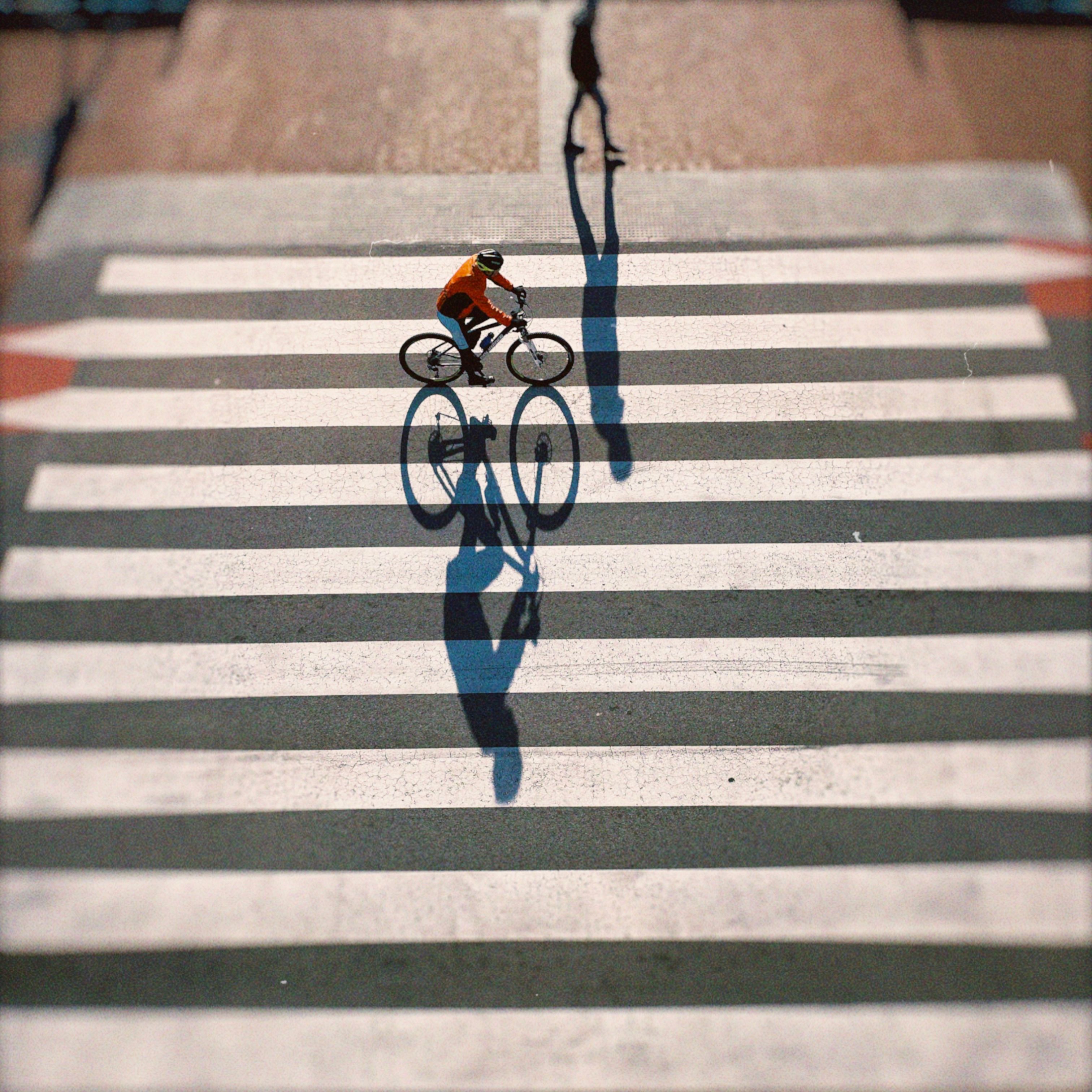 A cyclist crosses a striped crosswalk in Tarragona, Spain, casting a long shadow in the early morning sunlight.