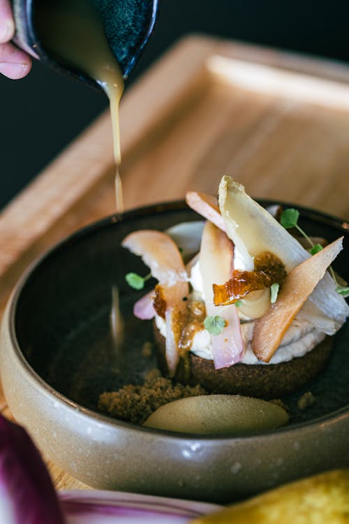 A person pouring sauce on a plate with food