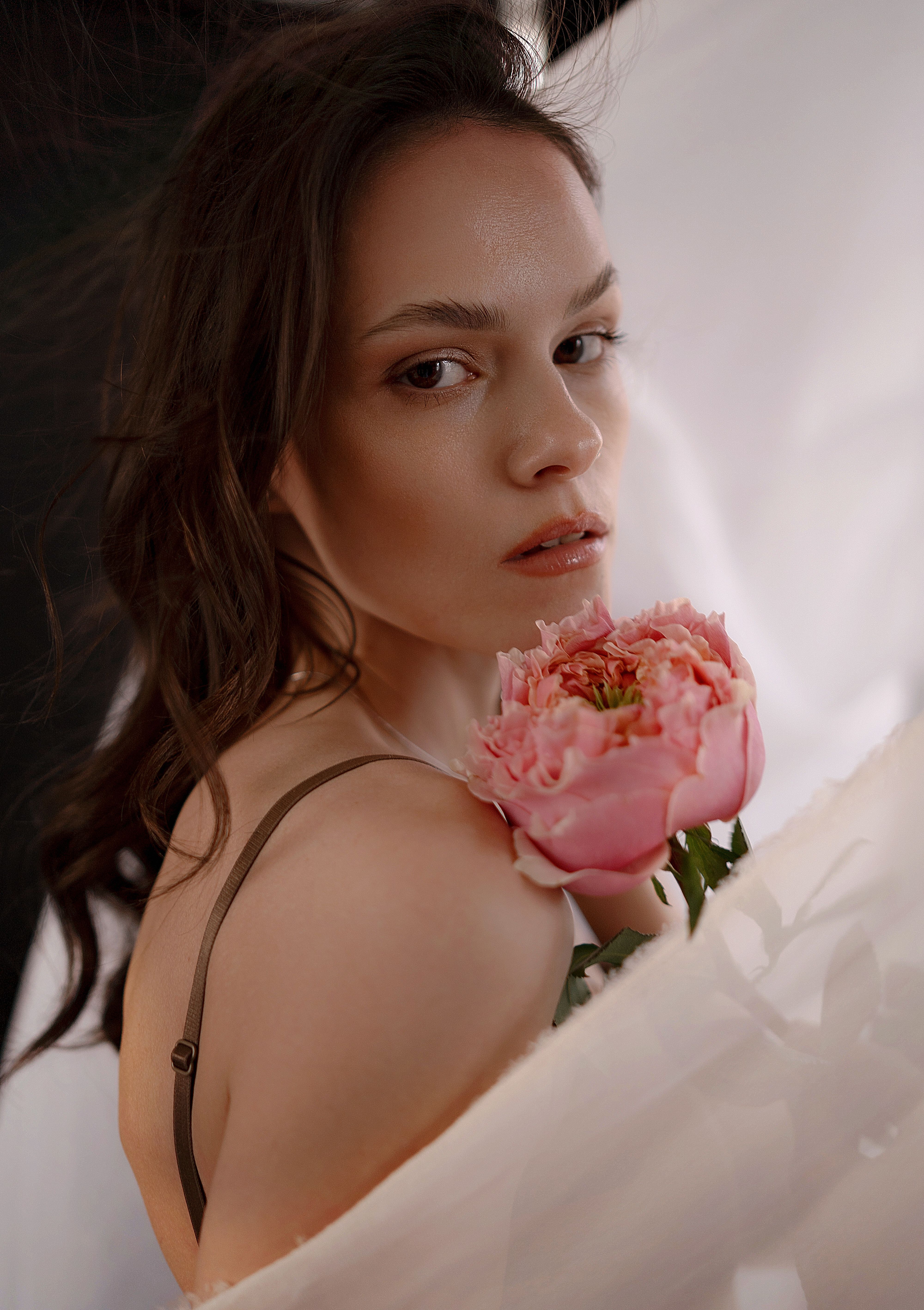 Elegant portrait of a woman with a pink peony, showcasing natural beauty and grace.