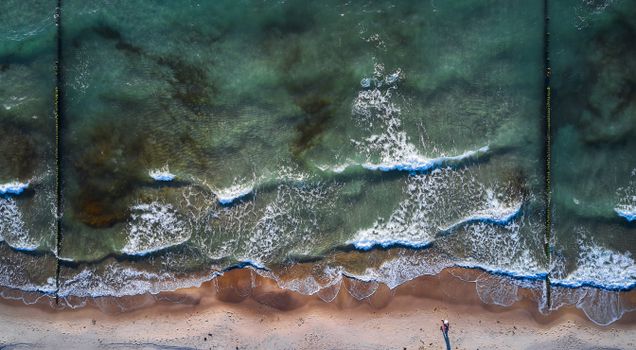 Captivating aerial view of sea waves crashing onto a sandy beach, creating a serene coastal scene.