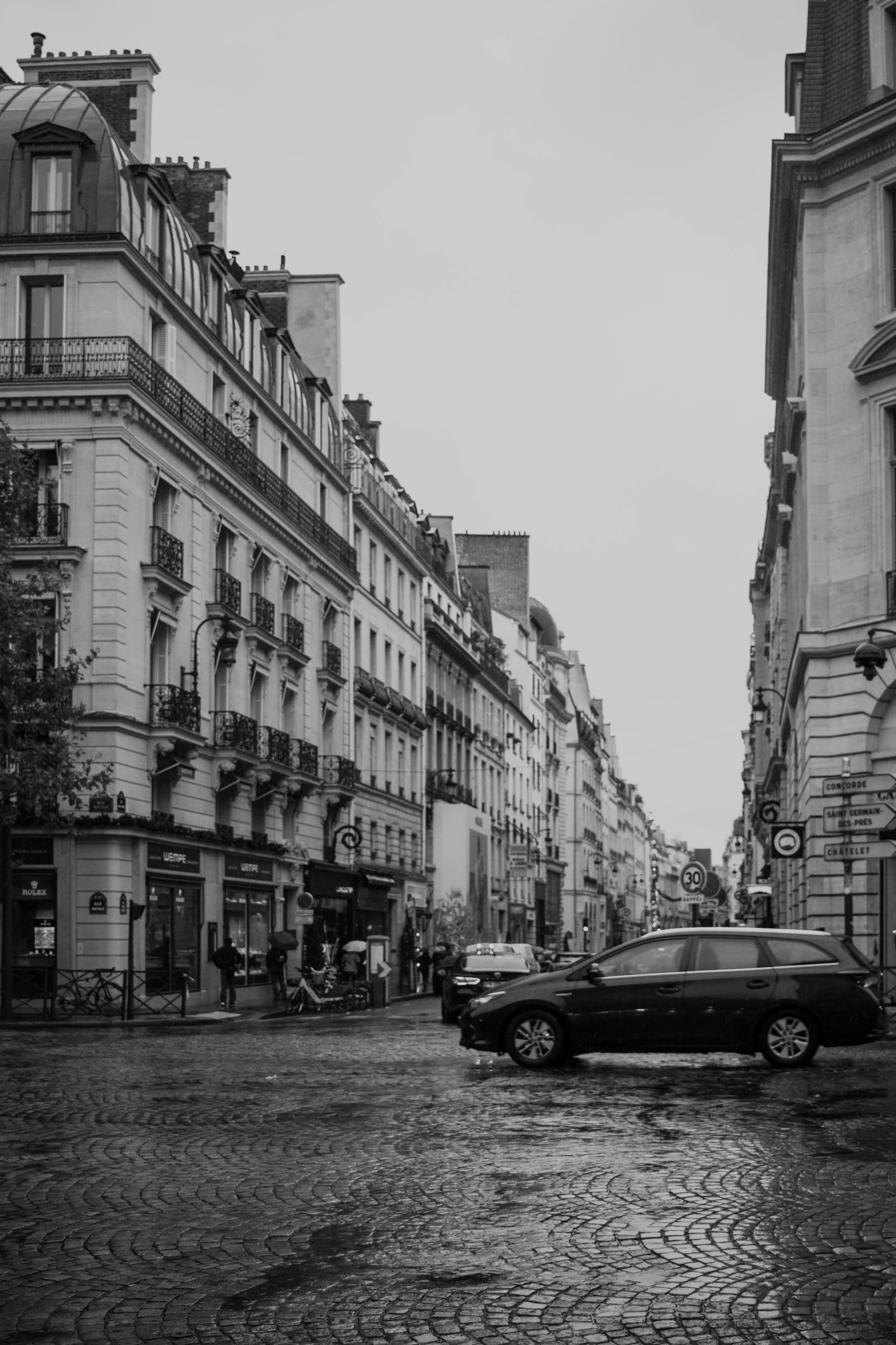 Black and white photo of a rainy Paris street with classic architecture and cobblestone paving.