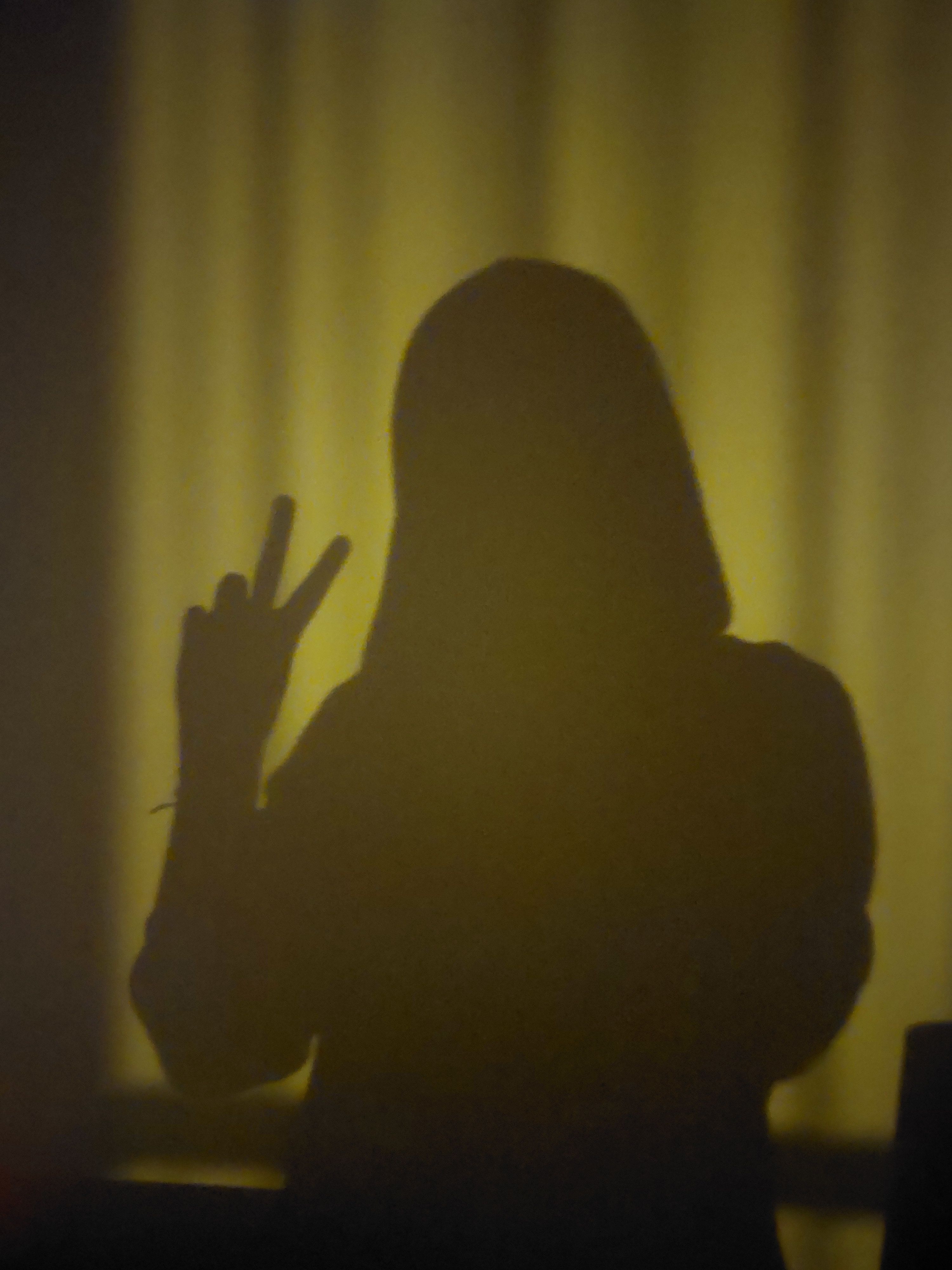 Mysterious silhouette of a person making a peace sign against a warm backdrop.