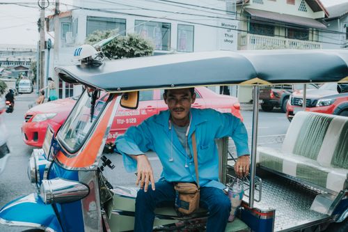 Free Tuk-tuk driver in blue shirt waits on busy Bangkok street, Thailand. Stock Photo