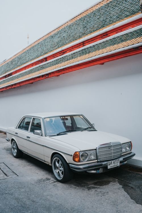 Free Classic white Mercedes W123 parked by a traditional temple wall in Bangkok, Thailand, showcasing urban vintage aesthetics. Stock Photo