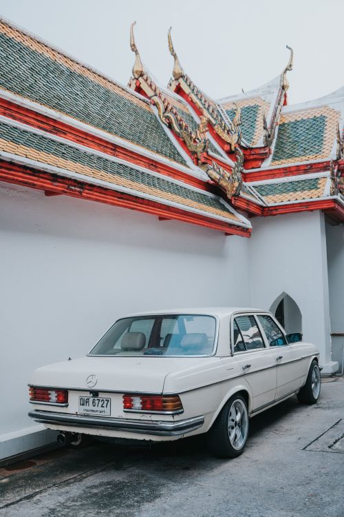 Free Classic white car parked next to a colorful Thai temple structure in Bangkok. Stock Photo