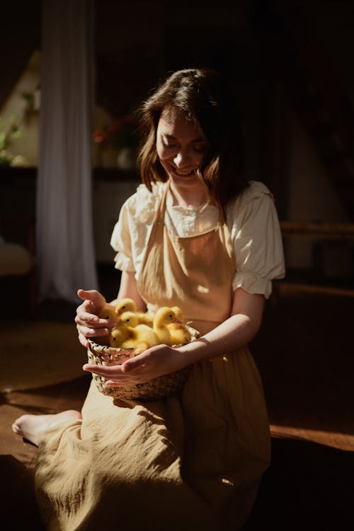 Young Woman Sitting on the Floor and Holding Ducklings in a Basket 