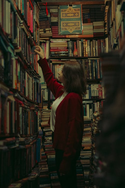 A woman is reaching for books in a library