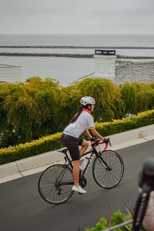 Free A female cyclist riding on a coastal road overlooking the ocean, showcasing fitness and adventure. Stock Photo