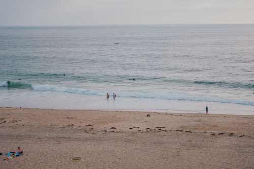 Free A serene beach scene with people enjoying the ocean waves under a calm sky. Stock Photo