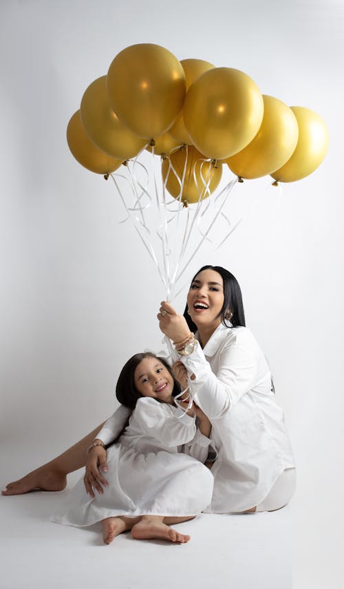 Smiling Mother and Daughter Sitting and Holding Balloons