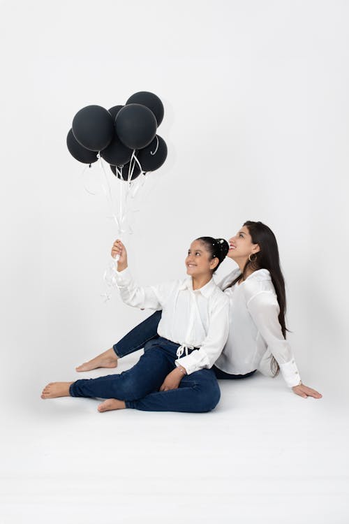 Two women sitting on the floor holding black balloons