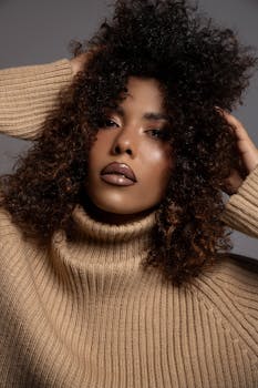 Close-up portrait of a woman with curly hair and bold makeup wearing a beige sweater.