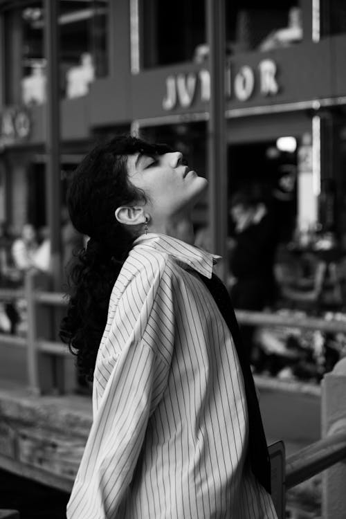 A woman in a striped shirt and tie is leaning against a railing