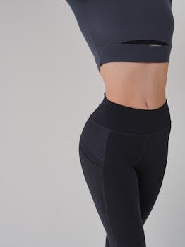 Close-up of woman in fitness attire, showcasing toned stomach and sweatpants in studio setting.