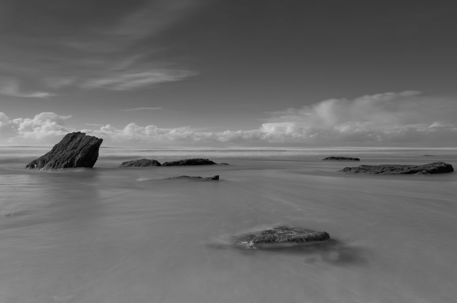 Long exposure black and white image of rocks and sea at Watergate Bay, England.