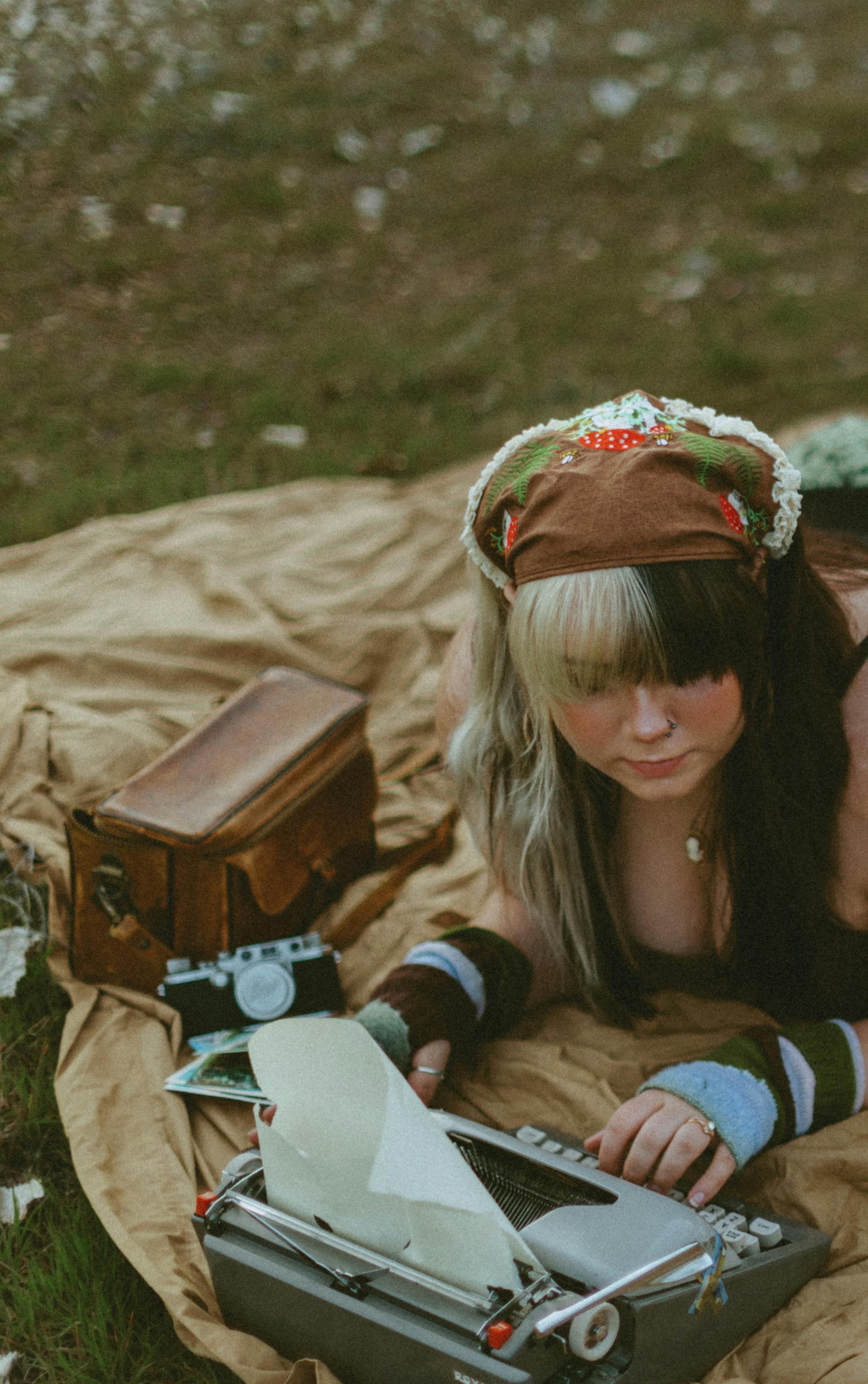 Bohemian woman typing on retro typewriter outdoors amidst vintage accessories.