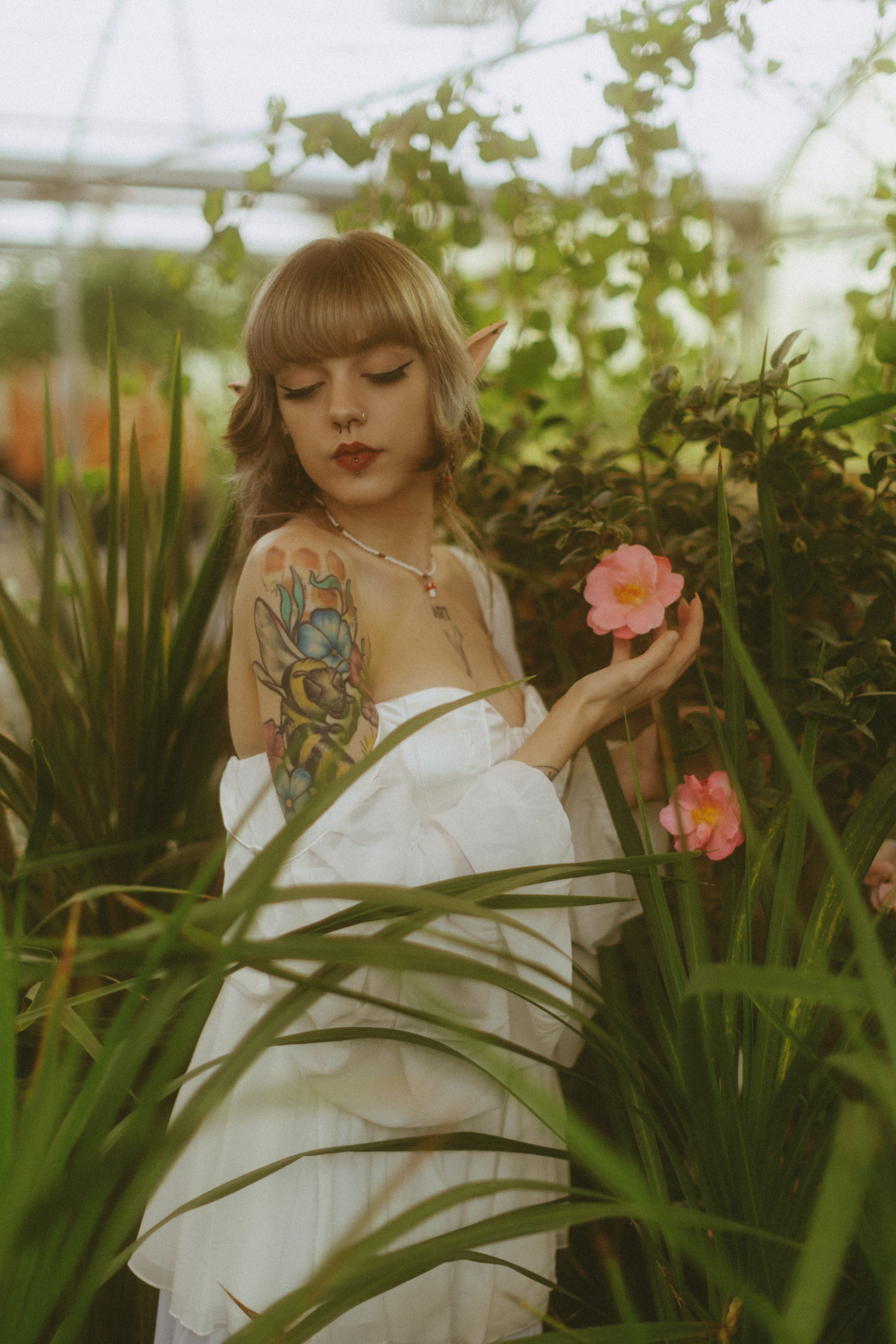Woman dressed as an elf with floral tattoo in a lush garden setting.